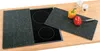 Two granite cutting boards are placed on a wooden countertop next to an induction stovetop. One board covers part of the stovetop, while the other is to the side with a yellow bell pepper, a red bell pepper, and a knife on it. Two small white containers ar Produktbild-Vorschau
