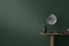 A dark green wall serves as the backdrop for a wooden table displaying decorative items and a book. Produktbild-Vorschau