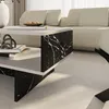 A close-up view of a modern coffee table with a marble black and white pattern, placed in a living room setting with a sofa in the background. Anteprima dell’immagine prodotto