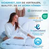 A woman is sitting on a bed with a white duvet, touching it. Produktbild-Vorschau