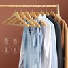 Wooden hangers holding various clothing items like dresses, shirts, and jackets. Produktbild-Vorschau