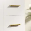 A close-up view of two gold handles on a white cabinet. Produktbild-Vorschau
