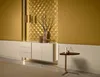 A modern living room with a white sideboard against a gold geometric wall, decorated with a vase and branches. A small triangular side table with decorative items is placed to the right. Anteprima dell’immagine prodotto