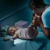 A mother is kissing her baby's feet on a changing table at night, with a small night light illuminating the scene. Voir les images du produit