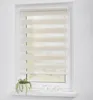 A close-up view of a window with a duo-roller blind installed. A small potted plant and three glasses are on the windowsill. Produktbild-Vorschau