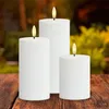 Three white LED candles with flickering flames are arranged on a wooden table outdoors. Produktbild-Vorschau