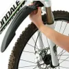 A person's hand is shown attaching a black bicycle fender to the front fork of a mountain bike. Podgląd zdjęcia produktu