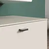 A close-up view of a drawer handle on a beige cabinet against a green wall. Produktbild-Vorschau