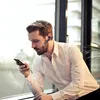 A man in a white shirt is using a smartphone and wearing a wireless headset. Produktbild-Vorschau