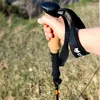 A hand holding a trekking pole in an outdoor setting with grass and trees. Náhled obrázku produktu