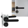 A close-up view of a black door lock mechanism and a black door handle set, with a blurred background of a modern interior. Produktbild-Vorschau