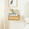 A wooden floating shelf with a cane drawer front is mounted on a white wall next to a bed. The shelf holds decorative items including books, a vase with flowers, and a small sculpture. Podgląd zdjęcia produktu