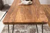 A close-up view of a wooden dining table with a chair and rug in the background. Produktbild-Vorschau