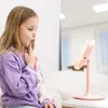 A young girl is sitting on a couch and looking into a pink makeup mirror. Voir les images du produit