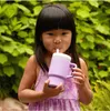A young girl drinks from a purple sippy cup outdoors. Produktbild-Vorschau