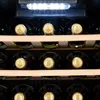 Interior view of a wine cooler with several bottles of wine lined up on wooden shelves. LED lights are visible at the top. Produktbild-Vorschau