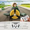 A child is riding in a toy airplane on a road, with a remote control in the foreground. Voir les images du produit