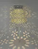 A white table lamp with a patterned shade is placed on a surface, casting decorative shadows on the wall and floor. Produktbild-Vorschau