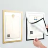 Two framed documents are shown on a wall, one gold and one black. A person's hands are shown manipulating the black frame. Anteprima dell’immagine prodotto