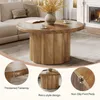 A round wooden coffee table is placed in a living room setting with a sofa and a fireplace in the background. Produktbild-Vorschau