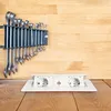 A set of wrenches is mounted on a wooden wall above a white retractable power outlet with two sockets and a USB port, all resting on a wooden surface. Produktbild-Vorschau