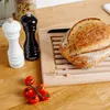 A bread cutting board with a loaf of bread, salt and pepper shakers, and cherry tomatoes on a wooden surface. Produktbild-Vorschau