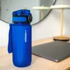 A blue Wessper water bottle is placed on a wooden desk next to a laptop. A lamp and a mirror are visible in the background. Podgląd zdjęcia produktu