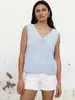A woman is posing in front of a textured wall, wearing a light blue crochet top and white shorts. Produktbild-Vorschau