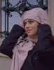 A woman wearing a pink beanie and scarf, with her hands on the beanie. Produktbild-Vorschau