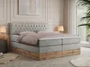A bedroom scene featuring a large boxspring bed with a tufted headboard and a wooden base, set against a wall with decorative molding and a large window with sheer curtains. Produktbild-Vorschau