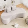 A modern, curved sofa is placed on a rug in a well-lit room, with a white dresser and a plant in the background. Náhľad obrázku produktu