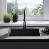 A modern kitchen sink with a black faucet and plants on the windowsill. Náhled obrázku produktu