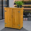 A wooden storage cabinet with two doors is shown on a patio, with potted plants on top and a blurred background of a modern outdoor space with lighting. Anteprima dell’immagine prodotto
