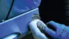 A gloved hand is cleaning a blue surface with a white cloth. Produktbild-Vorschau