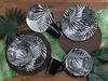 A set of black and white patterned plates and mugs arranged on a wooden surface with tropical leaves. Náhľad obrázku produktu
