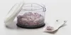 A manual chopper filled with chopped red onions, with its lid open and resting beside it. A small white dish with a few chopped onions is placed to the right. Produktbild-Vorschau