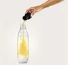 A hand is pouring a yellow liquid from a black cap into a clear bottle with a white base. Podgląd zdjęcia produktu
