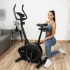 A woman is posing next to a stationary exercise bike in a home gym setting. Náhľad obrázku produktu