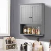 A gray wall-mounted cabinet with two doors and an open shelf below, containing jars of food items. A window is visible on the left, and a countertop with various kitchen items is below the cabinet. Podgląd zdjęcia produktu