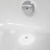 A close-up view of a white bathtub with a chrome overflow drain cover and a white drain stopper with a chrome center. Voir les images du produit