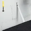 A close-up view of a white brick wall with a screw and wall plug on the left, and a white strap attached to the wall on the right. A dark fabric item is visible at the bottom. Náhled obrázku produktu