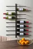 A wall-mounted wine rack holding several bottles of wine, with a bowl of oranges on a table in the foreground. Náhled obrázku produktu