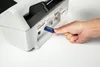 A hand inserts a USB drive into the back of a Brother scanner. Voir les images du produit