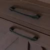A close-up view of two black drawer pulls on a dark wood-grained surface. Podgląd zdjęcia produktu