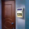 A solar-powered house number light is mounted on a wall next to a wooden door. Produktbild-Vorschau