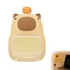 A cute capybara-shaped alarm clock with a night light function is shown against a white background. A smaller inset image shows the alarm clock lit up on a desk next to a laptop. Produktbild-Vorschau