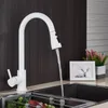A white kitchen faucet with a pull-down sprayer is shown in use, with water flowing into a dark sink. A small framed picture and a potted plant are visible on the counter. Náhľad obrázku produktu