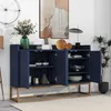 A navy blue sideboard with gold legs is displayed in a room with a painting and a plant. Náhled obrázku produktu