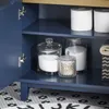 Close-up view of the interior of a blue bathroom cabinet, showing storage jars, toilet paper, and a folded towel. Produktbild-Vorschau