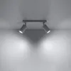 A ceiling light fixture with two adjustable spotlights is mounted on a white ceiling, casting light downwards onto a white wall. Náhled obrázku produktu